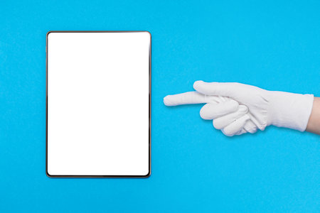 Digital tablet on blue background. A gloved hand points a finger at the tablet. Mock up. The concept of digital devices and communication.の写真素材