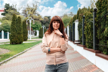Portrait of a young, confident woman with her tattoed arms posing at the street. In the background is an park. The concept of successful people.の写真素材