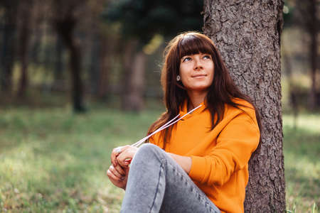 Portrait of a beautiful young woman sitting in the grass by a tree and posing. Recreation at the park.の写真素材