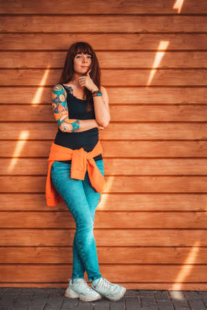 A young beautiful woman with tattoos on her arm, posing near a wooden wall. Vertical orientation.の写真素材