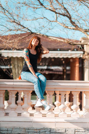 A young woman sits on the balustrade smiling sweetly. Vertical orientation. Outdoor.の写真素材