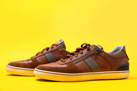 Pair of male's new sneakers made of brown leather on a yellow background. Copy space.の写真素材