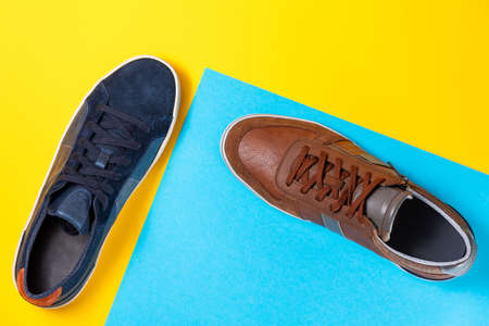 Two man's new stylish sneakers made of blue and brown leather on a yellow-blue background. Flat lay. Copy space. Concept of shopping and sales.の写真素材