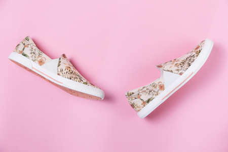 Pair of female's new stylish slip-ons with floral ornament on a pink background. Flat lay. Copy space. Side view of shoes.の写真素材