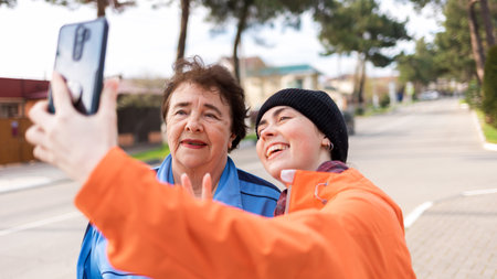 Grandmother and granddaughter smile and take a selfie on their smartphone. Outdoor. International Day of Older Persons.の写真素材