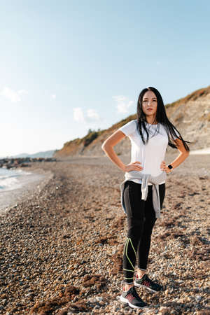 Concept of sport and healthy lifestyle. A young woman in sportswear, posing on a rocky beach, against the mountains. Copy space. Vertical.の写真素材