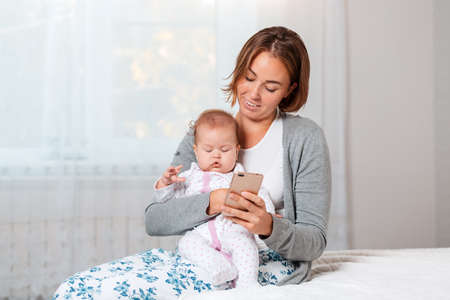 A mother holds a sleeping child in her arms and shows him something on her smartphone. Close-up...
