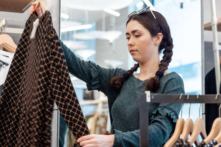 Portrait of a young Caucasian woman looking for clothes in a store. The concept of consumerism.
