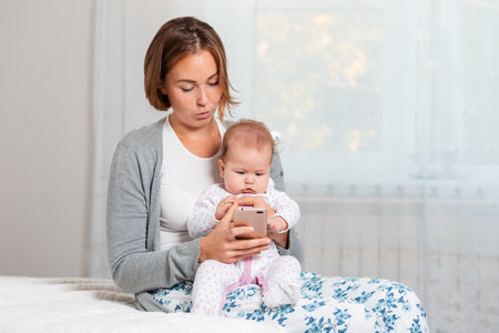 A mother holds a child in her arms and shows him something on her smartphone. Copy space. The...