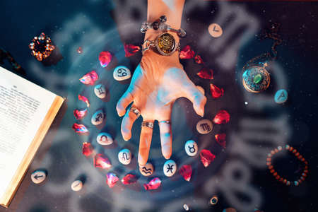 Astrology and horoscope. A woman's hand conjures stones with the signs of the zodiac, laid out in a circle and decorated with rose petals. The concept of divination and magic.の写真素材