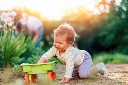 Smiling baby girl playing with a plastic toy cart at the summer garden. Concept of happy children's day.の写真素材