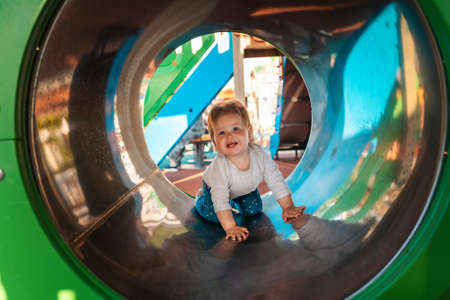 Funny caucasian baby girl playing on the playground, crawls in a tube. Outdoors. Concept of autism.の写真素材