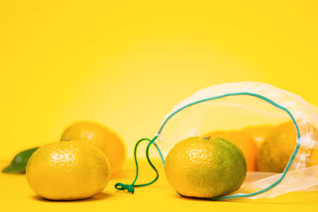 Eco-friendly. Fresh tangerines in reusable eco friendly mesh bag on yellow background. Copy space. Concept of zero waste.の写真素材