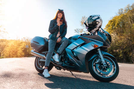 Motorcycle local travel. Young smiling woman in a leather jacket and sunglasses sitting on a...