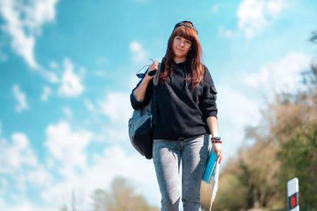 A pretty smiling girl hipster walks along the road with a map in her hands. Copy space. Concept of hitchhiking and local travel.の写真素材