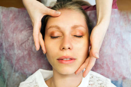 Young female face close-up, top view. The hands of the massage therapist makes a rejuvenating massage on the face. The concept of medicine and cosmetology.の写真素材