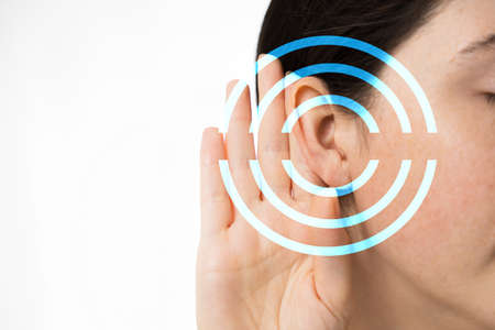 Hearing test. A young woman holds her hand to her ear, close-up. Isolated on a white background. Copy space. The concept of hearing health and deafness.の写真素材