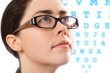 Healthy vision. Close up face of young beautiful woman in glasses looking at a diagram to check her vision. The concept of optical test and ophthalmology.の写真素材