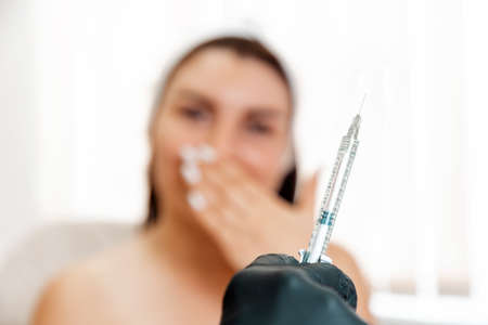 Plastic surgery in salon. Cosmetologist show syringe with medical, close up. Client fearing on the background, defocused. Concept of cosmetology.の写真素材