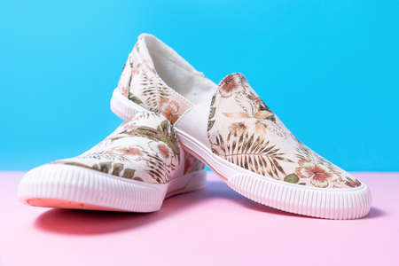 Pair of female's new stylish slip-ons with floral ornament on a pink-blue background. Copy space. Close up.の写真素材
