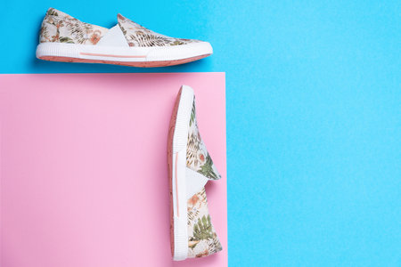 Pair of a new female's slip-ons made of floral pattern canvas on a pink-blue background. Flat lay. Copy space. Side view of shoes.の写真素材