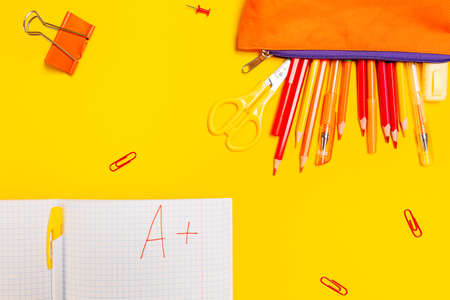 Education. Pencil box with pens and notebook with an excellent grade on a yellow background with...
