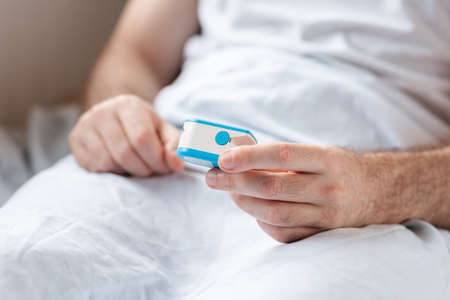 Health care. Close up of hands of hospitalized patient, lying at bed and holding a pulse oximeter....