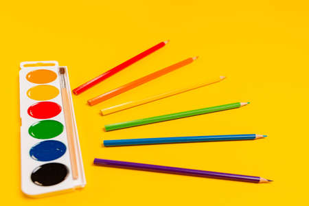Watercolors with a brush and with multicolored crayons on yellow background. Close up. The concept...
