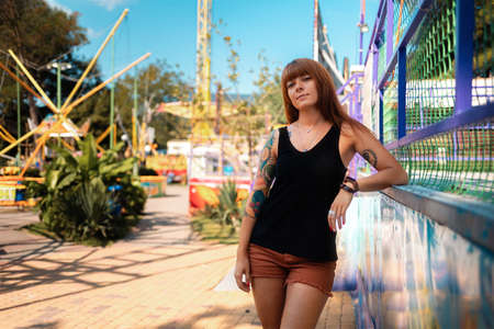 Summertime. Portrait of a beautiful young woman with tattoos posing in an amusement park. The...