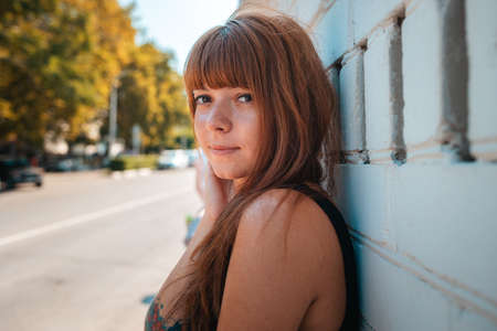Summertime. Portrait of young pretty smiling woman with a tattoo posing by the white wall. The...