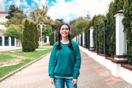 Smiling female student with pigtails stands on the street, at the entrance to the university. Outdoor, fence. The concept of admission of students to the university.の写真素材