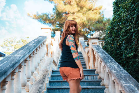 Travel and architecture. A young smiling woman with tattoos climbs the stone steps and turns to the...