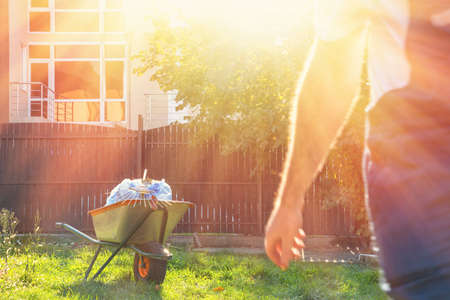 garden cart with garbage bags and rake on the background of a walking man in a gardener's uniform.in the bright sun.の写真素材
