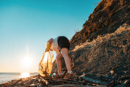 A volunteer activist collects garbage on a wild beach. Copy space. Cleaning of the coastal zone. The concept of Earth Day.の写真素材