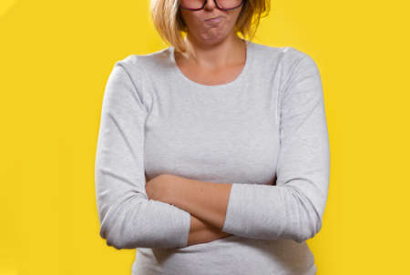 Emotions and psychology. The woman, a blonde with glasses, crossed her arms and pursed her lips with a disgruntled face. Close up.の写真素材