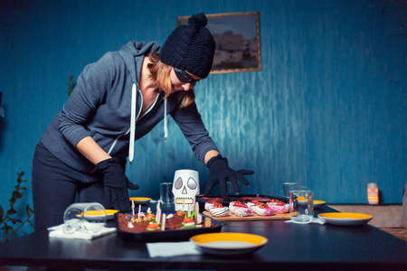 A woman in a robber's costume steals sweets from a holiday table. The concept of Halloween.の写真素材