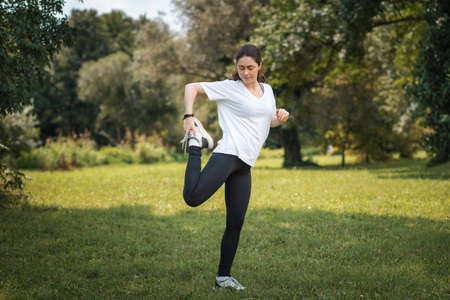 A young fit caucasian woman in sports clothes doing warmup at the park. The concept of wellness and...