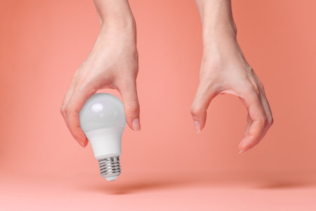 Breast Cancer Awareness Month. Female hands holding an electric light bulb on a pink background. Close up. The concept of oncology.の写真素材
