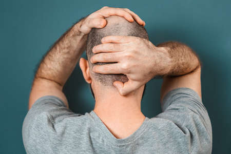 Self-doubt and inferiority complex. Baldy brunette man grabs his head with his hands. Rear view. Turquoise background. The concept of alopecia and baldness.の写真素材