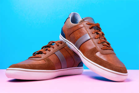 Pair of male's new sneakers made of brown leather laid out on a blue-pink background. Close up.の写真素材