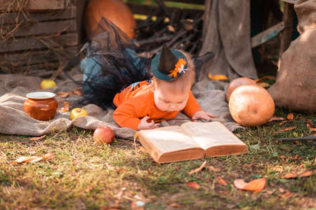 A toddler girl in a witch costume lying on the grass in kitchen-garden and plays with book. Halloween concept.の写真素材