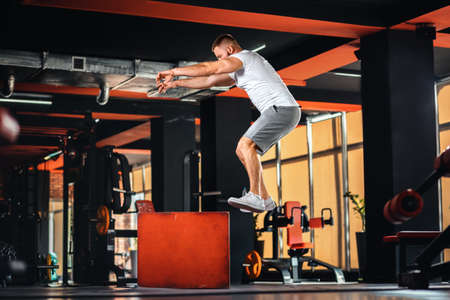 Young bearded athletic man training in the gym jumping at cube. Side view. The concept of fitness...