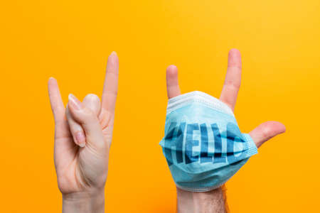 World Hello day. A female's hand and a male's hand with a mask on, fingers spread. Inscription on the mask Hello. Yellow background. The concept of protection from the virus.の写真素材