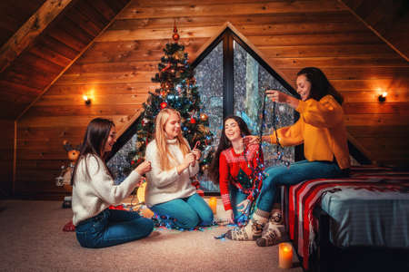 Christmas and new year. A group of young happy women socialize and untangle the lights. Scandinavian style interior.の写真素材