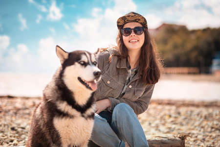Portrait of a young happy woman and a husky dog. In the background, the beach, the sea and the cloudy sky. Concept of care and protection of pets.の写真素材