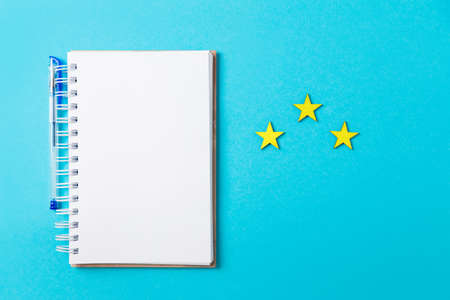 A white notebook with a pen on a blue background and three stars. Flat lay. Copy space. Rating concept.の写真素材