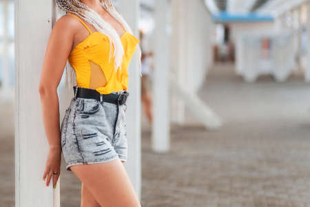 A slender woman in shorts and a yellow tank top poses at a pole. Waist close-up. The concept of slimness and health.の写真素材