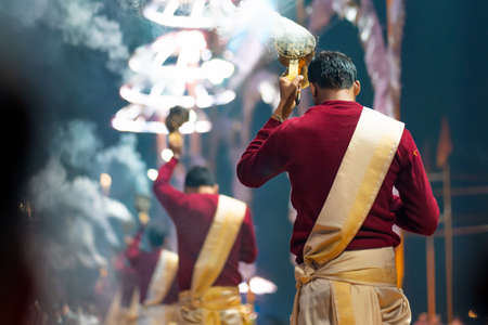 Sacred religious ceremony Arati in the temple. A group of people burn incense. Night. Rear view. Led umbrellas on the background.の写真素材