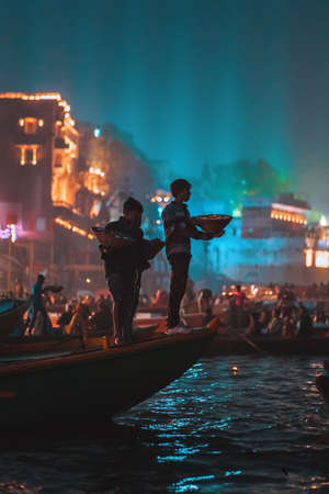 12/18/2019, Varanasi, India. A group of people with offerings in their hands, floating on a boat on the river. Night, religious holiday.のeditorial素材