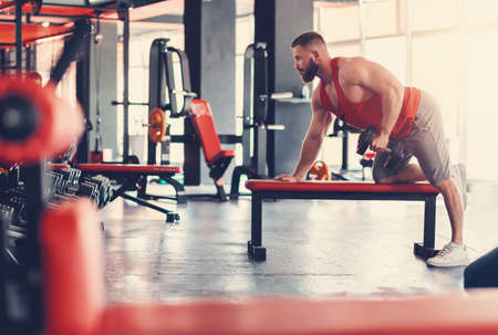 A young bearded athletic man trains with dumbbell in the gym. Side view. The concept of a wellness...